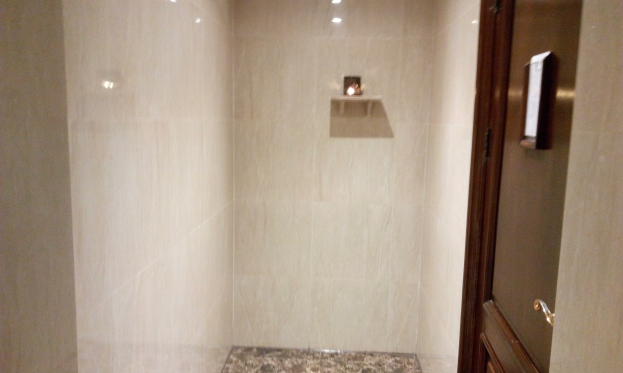 Ein Badezimmer mit einer Duschwanne mit Tür neben einer Toilette, mit einer Tür auf der rechten Seite; geflieste Wände und Deckenleuchten schaffen eine gemütliche Atmosphäre.