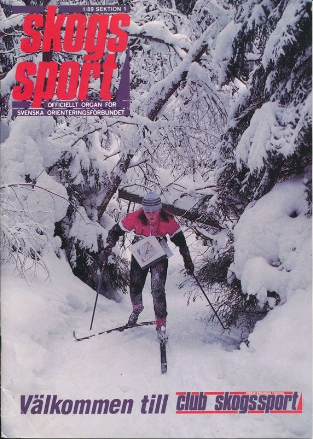 Eine Person mit einer Mütze und Ski-Stöcken fährt eine schneebedeckte Anhöhe hinunter, umgeben von schneebedeckten Bäumen, mit "Skogs Sport - Valkommen till Club Skogssport" unten.