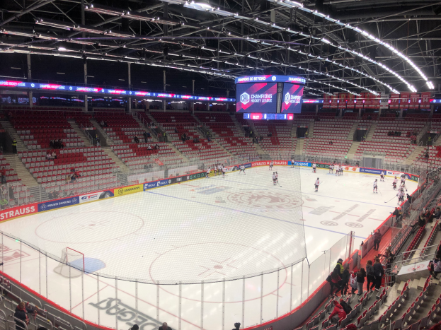 Ein Eishockeyspiel in einer großen Arena mit Zuschauern auf den Sitzplätzen und Stehplätzen, einem Zaun um die Eisfläche, einem Bildschirm mit der Aufschrift "St. Louis Blues vs Detroit Red Wings", Metallrahmen und einer Decke mit Deckenleuchten.