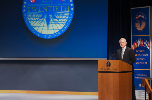 US-Außenminister Mike Pompeo, der einen schwarzen Blazer, ein weißes Hemd und eine schwarze Krawatte trägt, steht an einem Podium mit zwei Mikrofonen vor einer blauen Wand und spricht bei der 20. Internationalen Seemachtkonferenz, rechts von ihm ist ein Geländer.