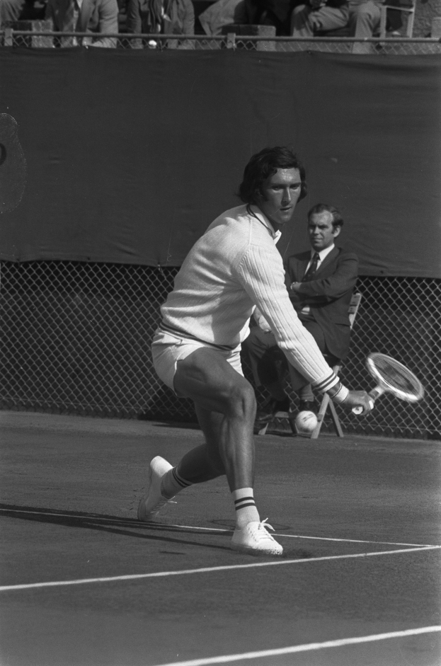 Eine professionelle Tennisspielerin in Sportbekleidung schlägt mit einem Schläger einen Ball während eines Matches, mit Zuschauern hinter einem Maschendrahtzaun sitzend.