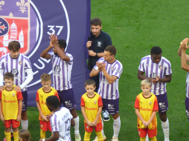 Junge Jungs auf einem Fußballfeld klatschen, mit einem Banner und Logos im Hintergrund.