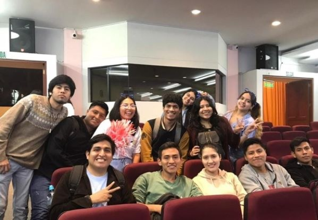 Gruppe von Menschen, die fröhlich in einem Kinosaal mit Wandlautsprechern und Deckenbeleuchtung posieren, wahrscheinlich auf einem Filmfestival.