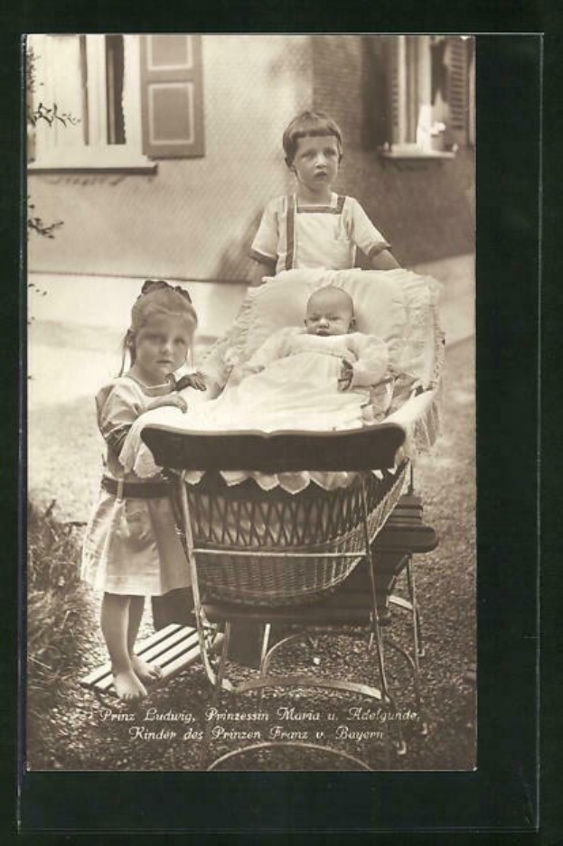 Schwarz-weiß-Foto von zwei Kindern, die neben einem Baby in einer Wiege stehen, mit einem Geb├Ąude und einer Pflanze im Hintergrund und Text unten.