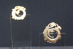 Goldene runde Ohrringe mit detaillierten Designs in einer durchsichtigen Glasvitrine präsentiert.