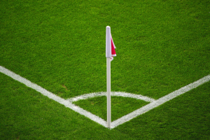 Ein Fußballfeld mit grünem Rasen, weißen Begrenzungslinien und einem Elfmeterpunkt, der durch einen weißen Pfosten mit einer roten und weißen Fahne markiert ist.