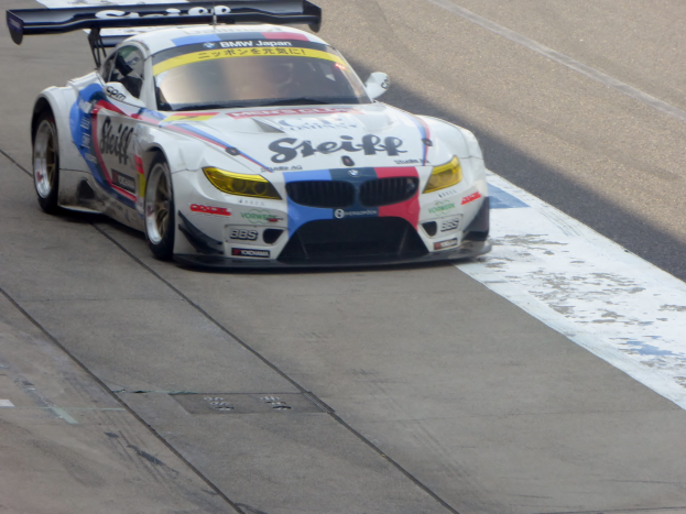 Ein strahlend blauer und weißer BMW Z4 GT3 Rennauto mit großen glänzenden Rädern auf einer Rennstrecke.