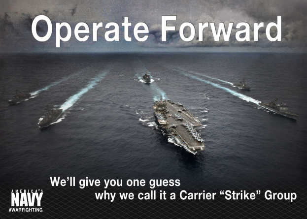 Plakat mit dem Text "Operate Forward - Wir verraten Euch, warum wir es Carrier Strike Group nennen" mit Schiffen auf dem Wasser und einem bewölkten Himmel im Hintergrund.