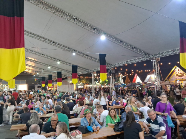 Eine große Gruppe von Menschen sitzt an Tischen unter einem Zelt auf dem Oktoberfest in München, Deutschland, mit Taschen und Gegenständen auf den Tischen und festlicher Dekoration im Hintergrund.
