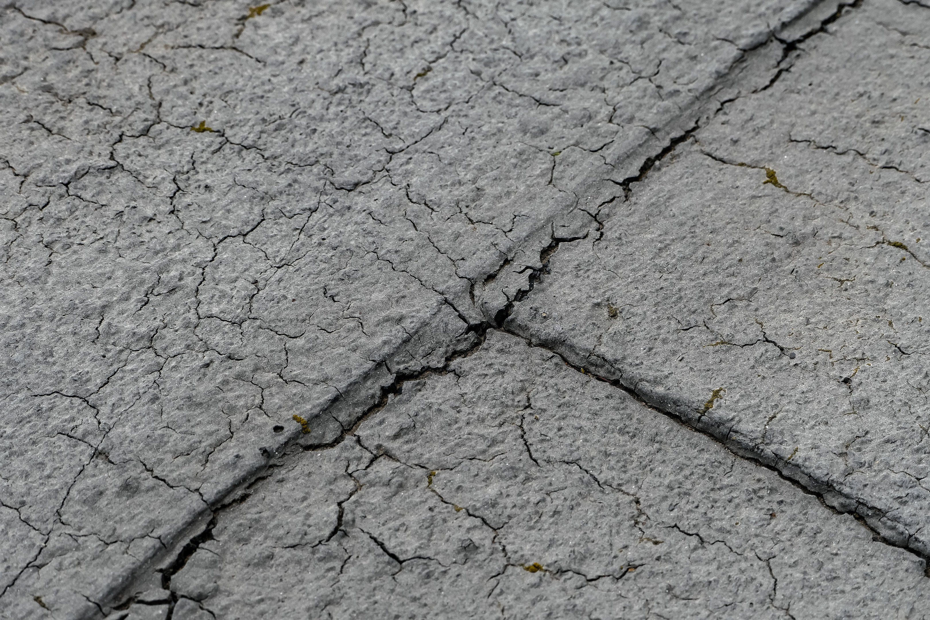 Nahaufnahme einer rissigen und verwitterten Straßenoberfläche mit tiefen, breiten Rissen und rauer, unebener Textur.