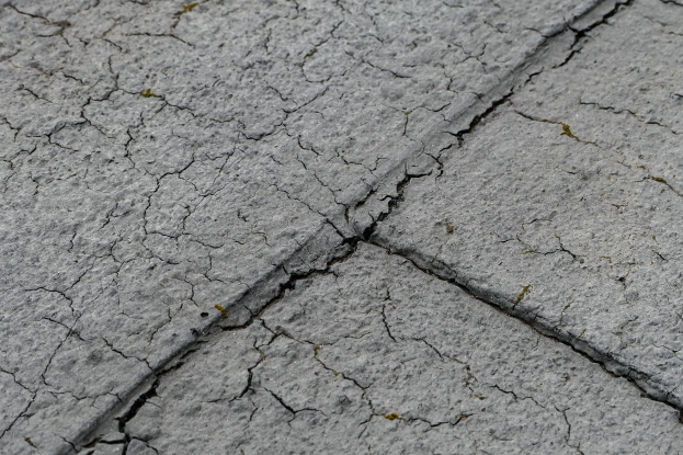 Nahaufnahme einer rissigen und verwitterten Straßenoberfläche mit tiefen, breiten Rissen und rauer, unebener Textur.